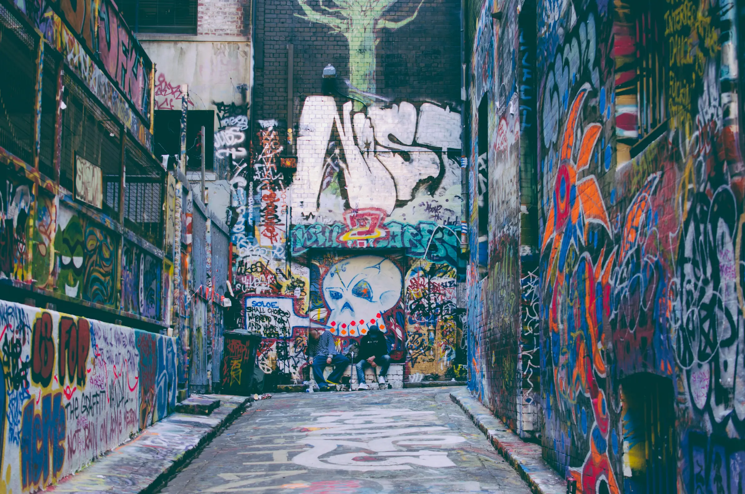 A cobbled bluestone laneway with every wall, door and window frame covered in street art and graffiti, running away between tall brick buildings